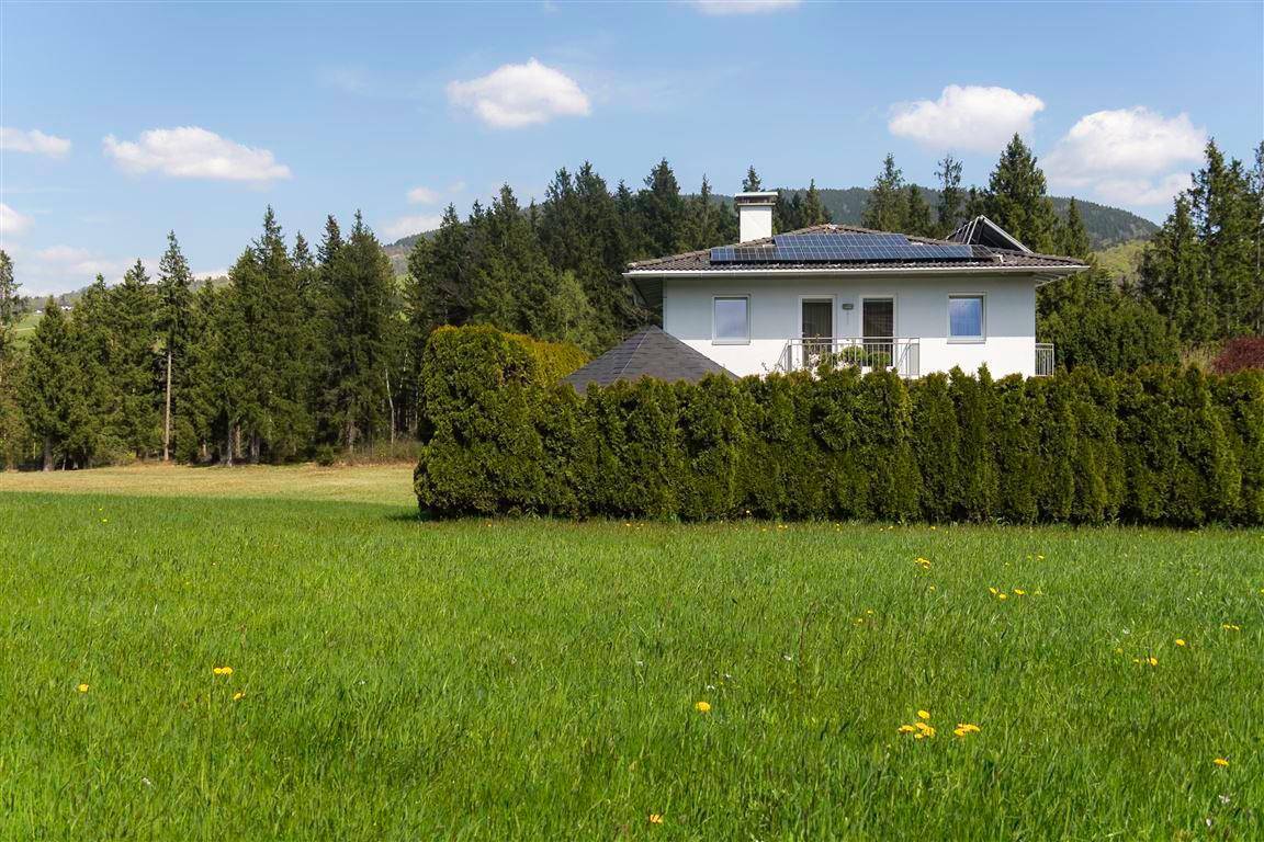 Modernes Wohnhaus mit Photovoltaikanlage, umgeben von grünen Feldern und Wald.