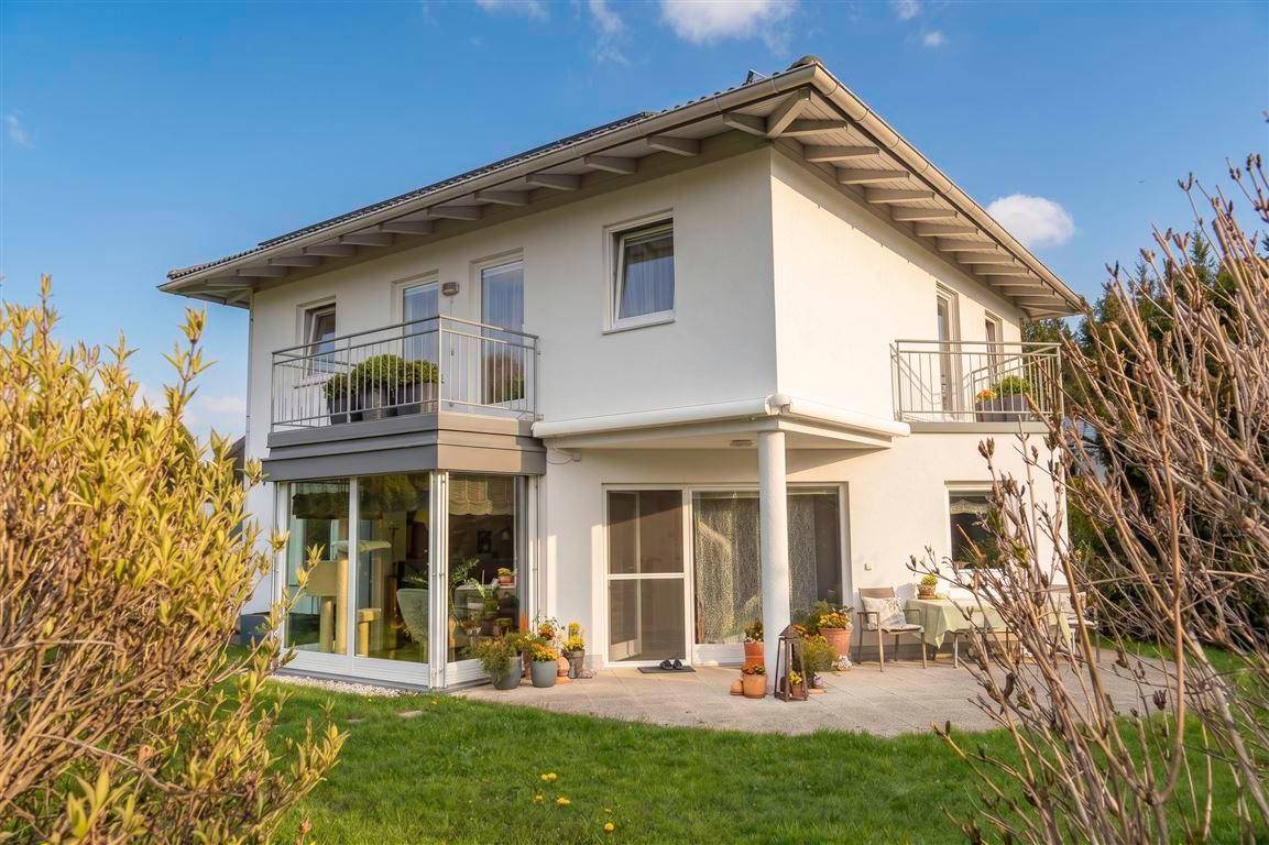 Rückansicht des Hauses mit Wintergarten, Terrasse und Balkon im Sonnenlicht.