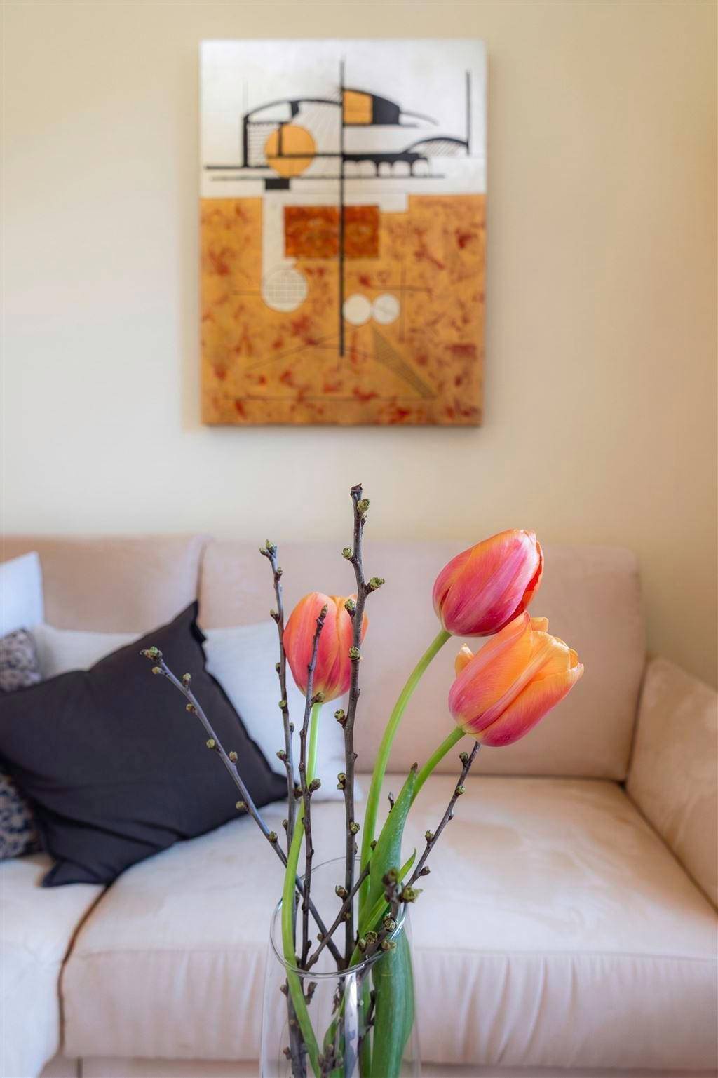 Nahaufnahme von orangefarbenen Tulpen vor einem beigen Sofa und abstrakter Kunst.