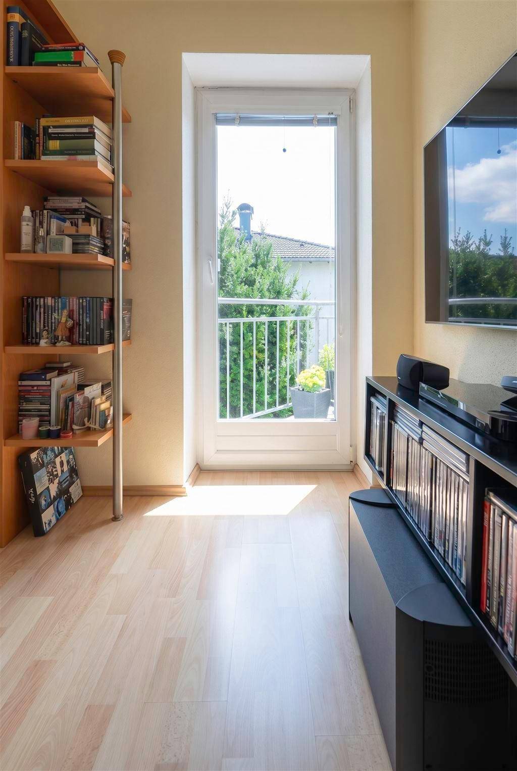 Heller Wohnbereich mit Bücherregal, Medienschrank und Zugang zu einem französischen Balkon.