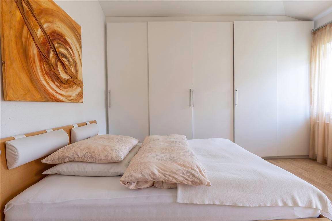 Schlafzimmer mit großem Kleiderschrank, hellem Bett und dekorativem Wandbild.