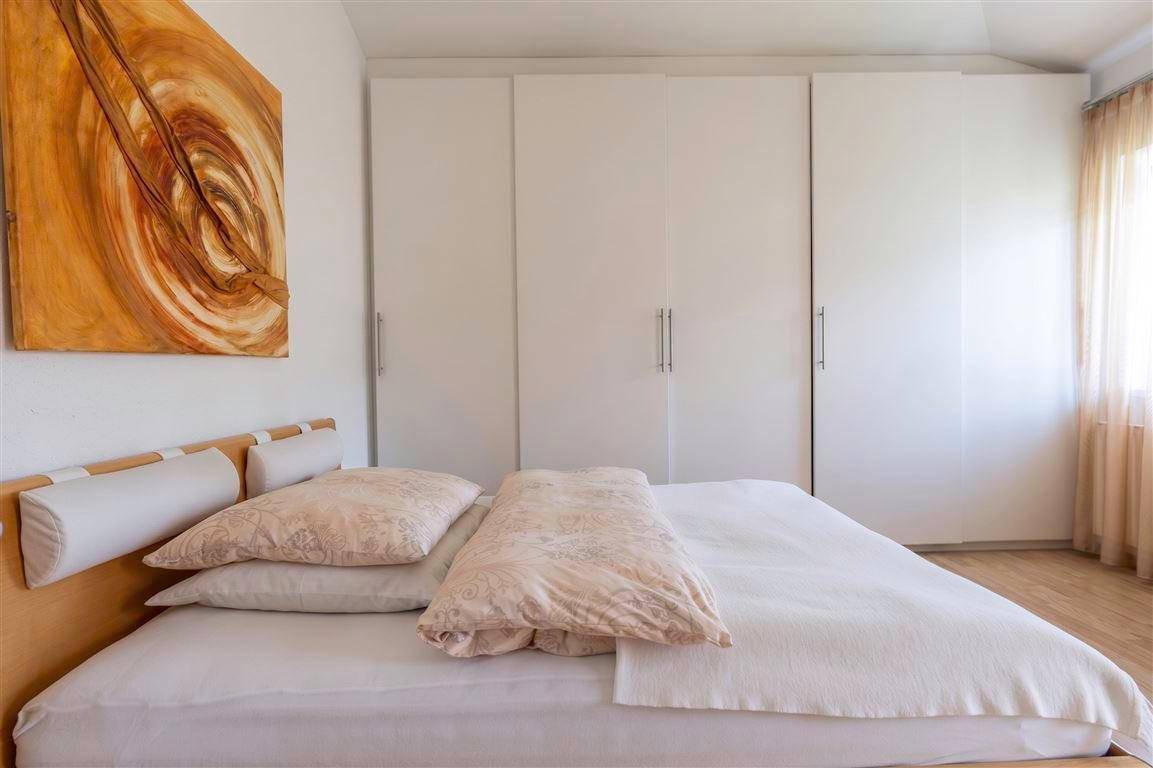 Ein gemütliches Schlafzimmer mit einem Holzbett, weißen Einbauschränken und einem modernen Kunstwerk.