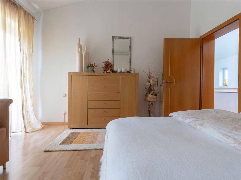 Helles Schlafzimmer mit Holzboden, einem Holzschrank und einem offenen Durchgang zu einem weiteren Raum.