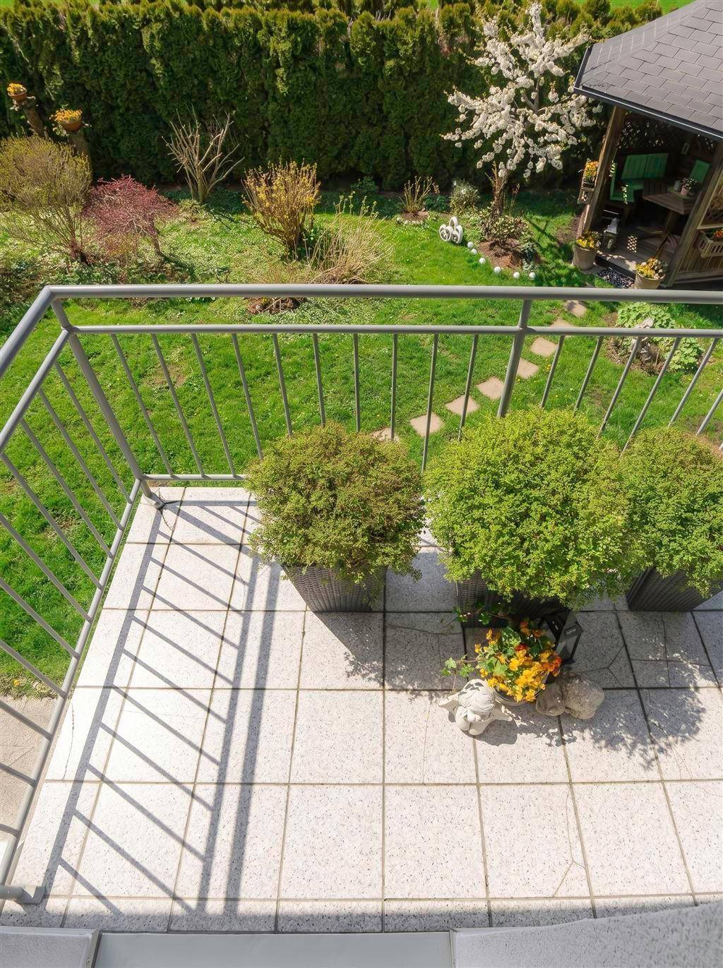 Blick vom Balkon auf den gepflegten Gartenbereich mit Rasen, Sträuchern und einem Gartenhaus.