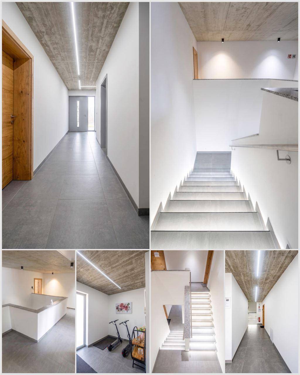 Moderner Flur und Treppenhaus mit indirekter Beleuchtung, Betondecke und Fliesenboden.