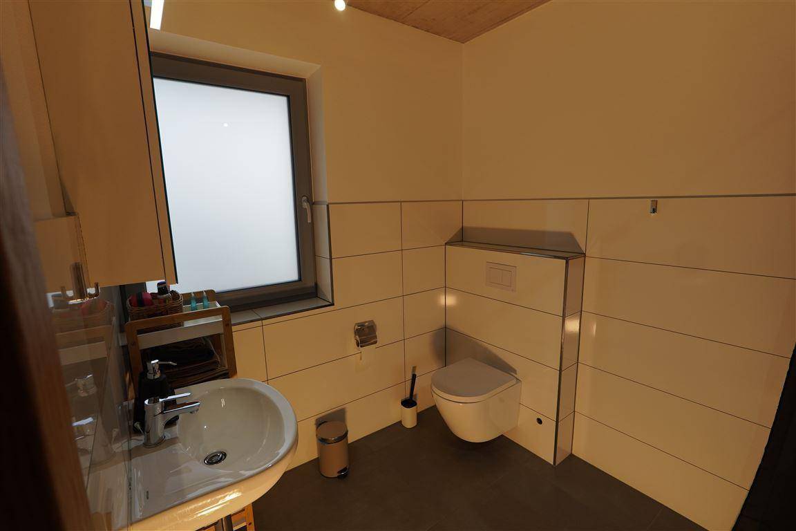 Modernes Badezimmer mit Fenster, Waschbecken und wandhängendem WC.