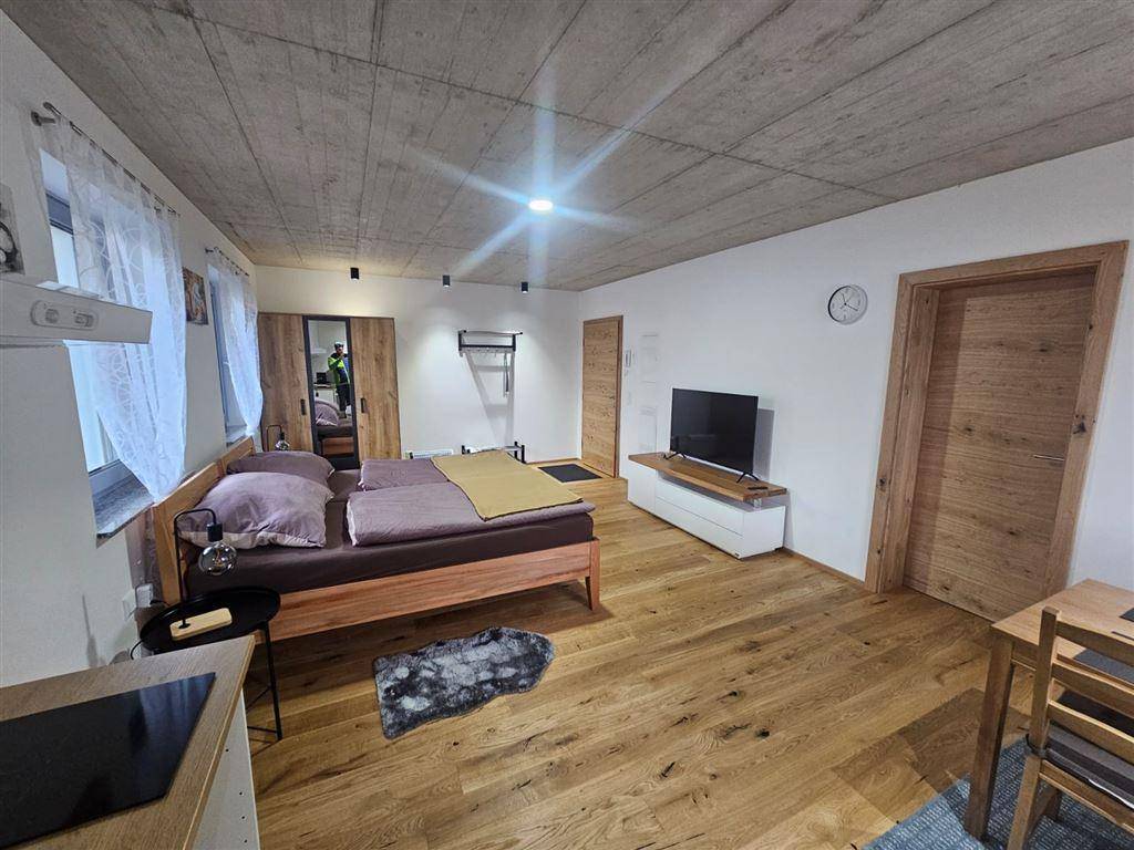 Schlafzimmer mit Holzbett, Holzboden, TV-Möbel und freiliegender Betondecke.
