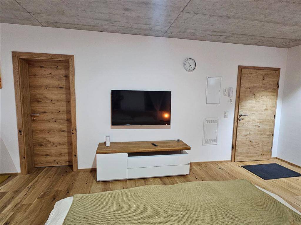Studio-Apartment mit Schlafbereich, Fernseher und Holztüren, die eine warme Atmosphäre schaffen.