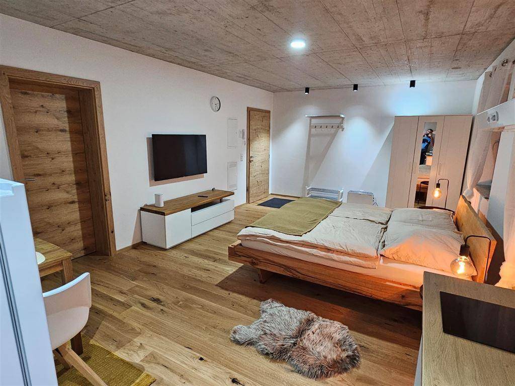 Modernes Schlafzimmer mit Holzboden, freiliegender Betondecke und integriertem TV-Bereich.