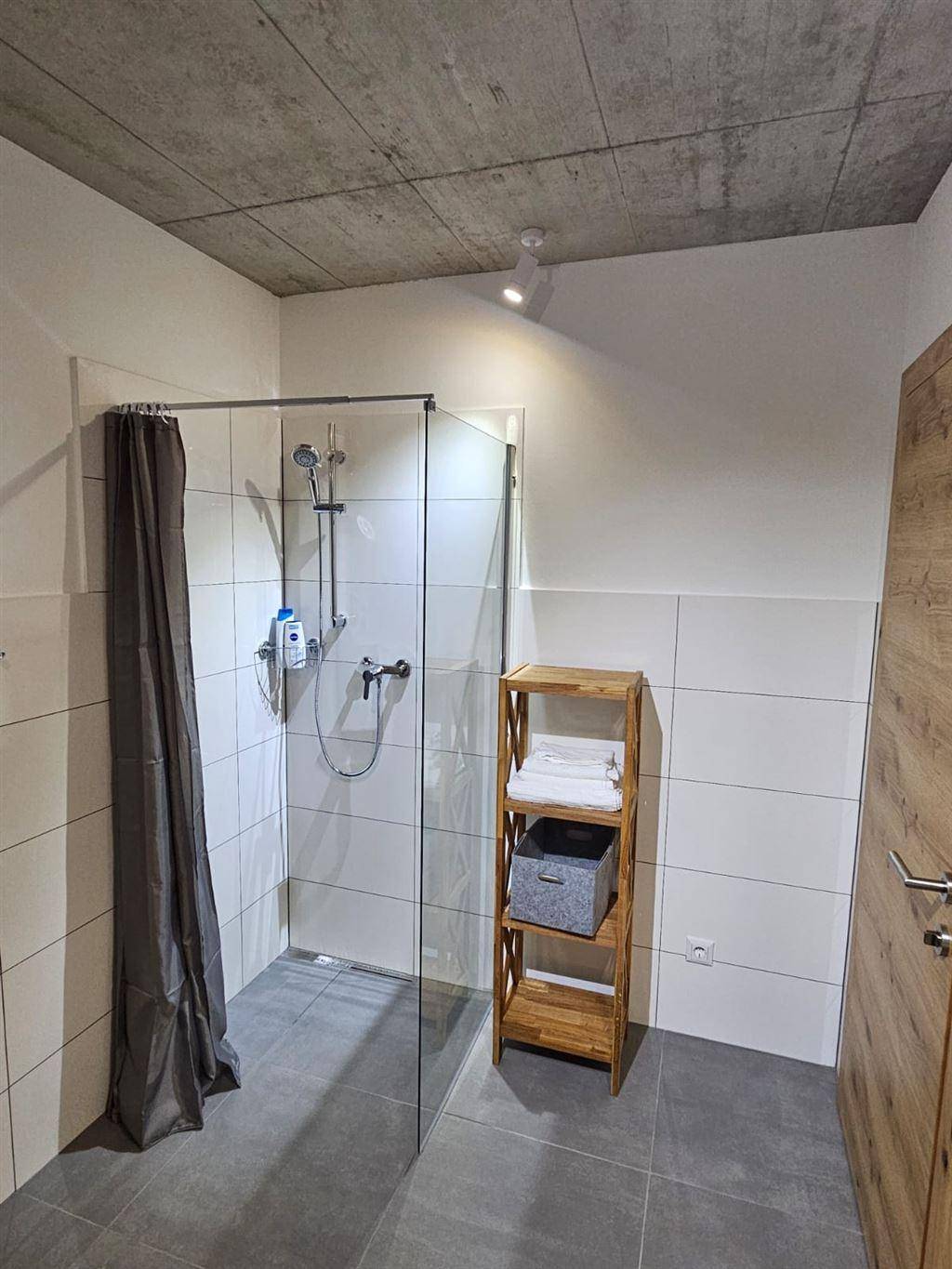Modernes Badezimmer mit ebenerdiger Dusche, weißen Fliesen und Betondecke.