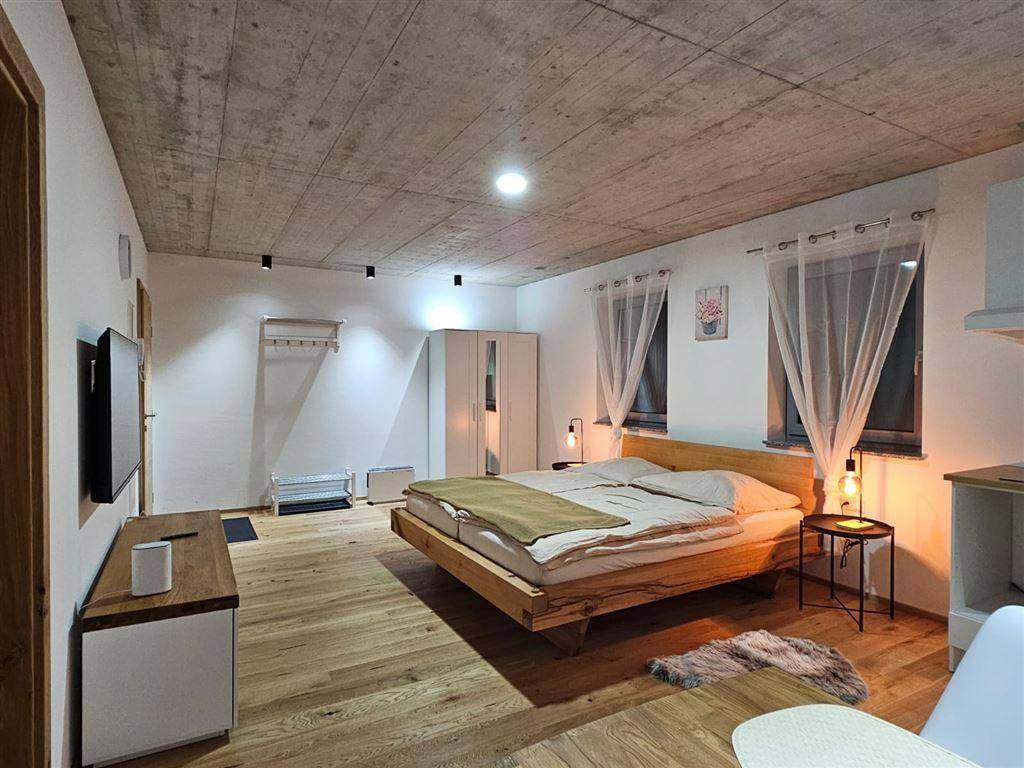 Helles Schlafzimmer mit Holzbett, Holzboden und freiliegender Betondecke, modern eingerichtet.