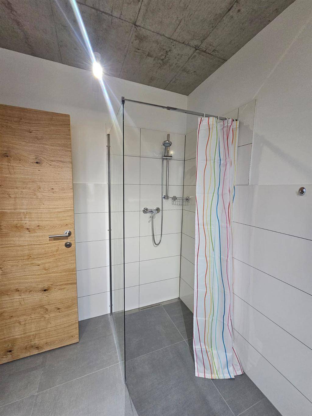 Duschbereich im Badezimmer mit Glasabtrennung und farbenfrohem Duschvorhang.