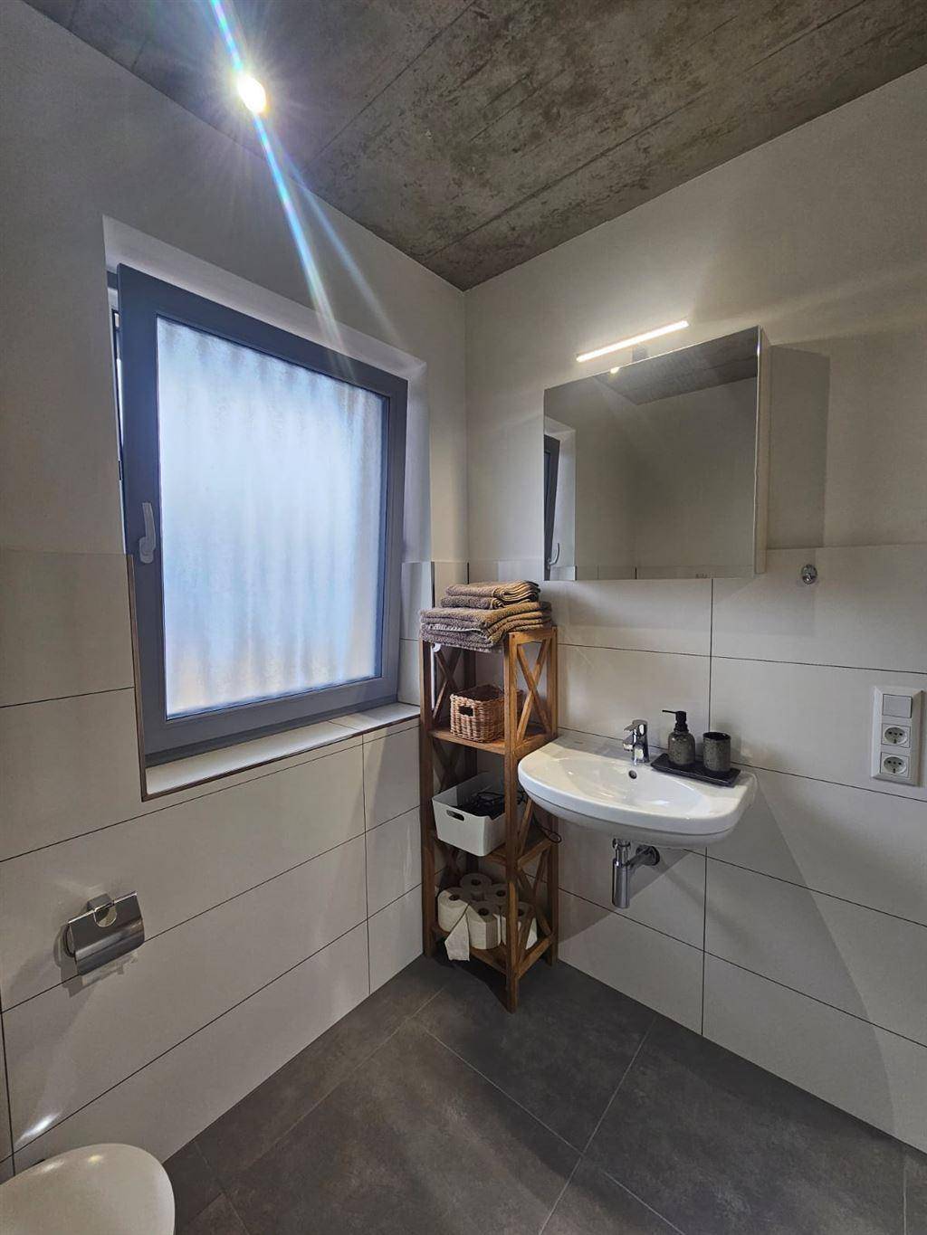 Badezimmer mit Waschbecken, Spiegelschrank und Fenster, modern gefliest.