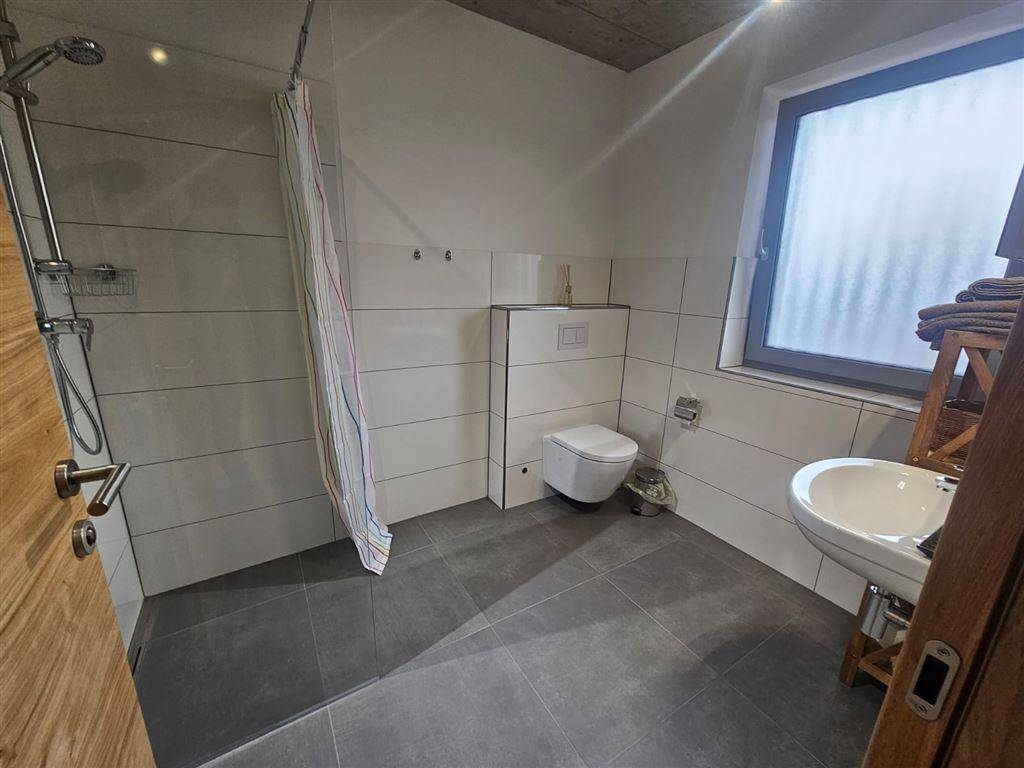 Helles Badezimmer mit Dusche, WC, Waschbecken und Fenster für Tageslicht.