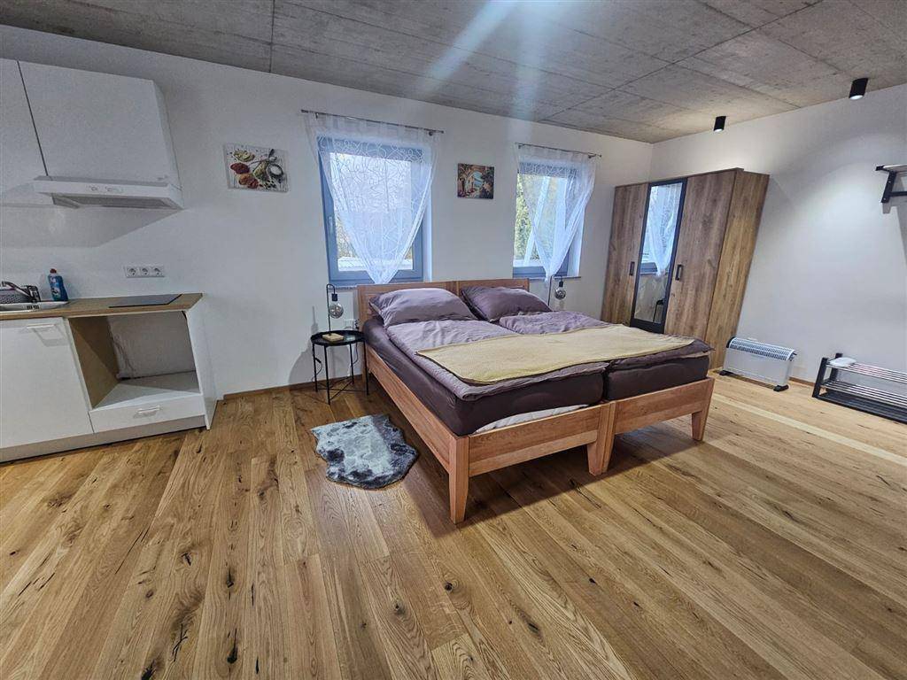 Schlafbereich mit Doppelbett, Kleiderschrank und kleiner Küchenzeile im Hintergrund.