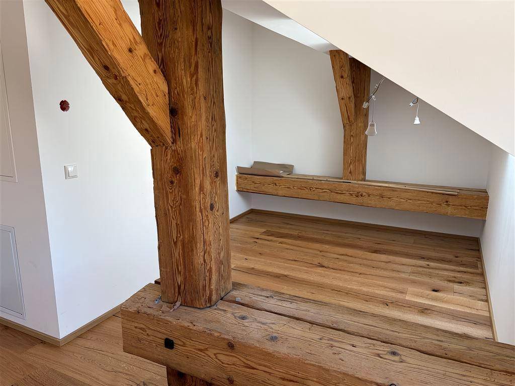 Detailansicht der massiven Holzbalken und des robusten Holzbodens in einem hellen Dachbodenraum.