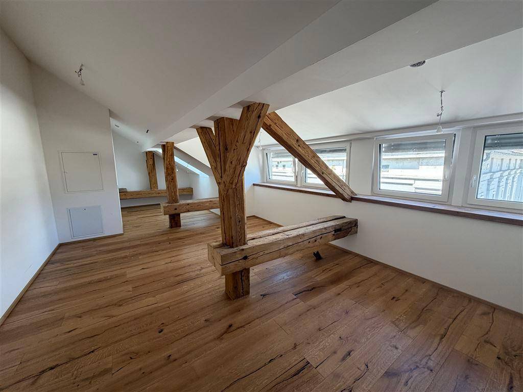 Heller Dachbodenraum mit rustikalen Holzbalken, hochwertigem Holzboden und Fenstern für natürliche Belichtung.