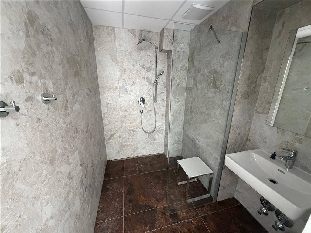 Modernes Badezimmer mit einer geräumigen begehbaren Dusche, eleganten grauen Wandfliesen und einem Waschbecken.