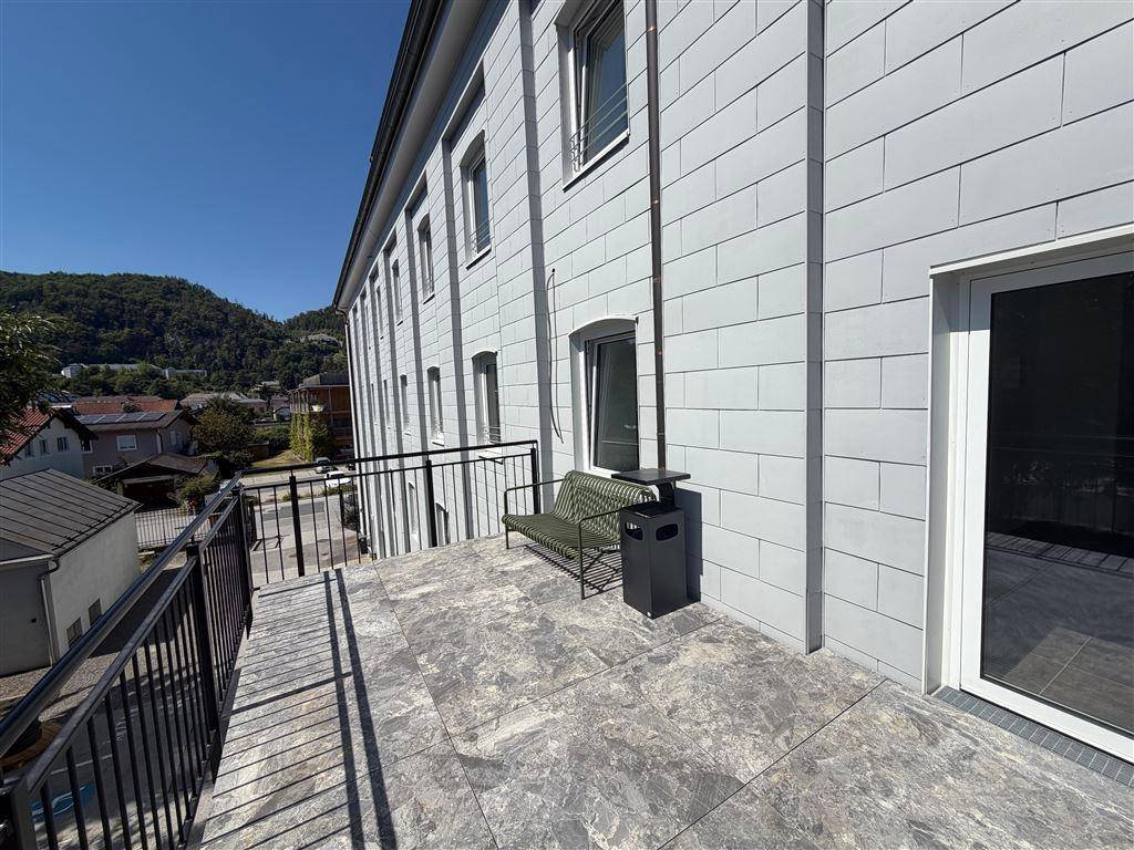 Breite Terrasse mit Fliesenboden und einer Sitzbank, angrenzend an die moderne Gebäudefassade mit Fenstern.