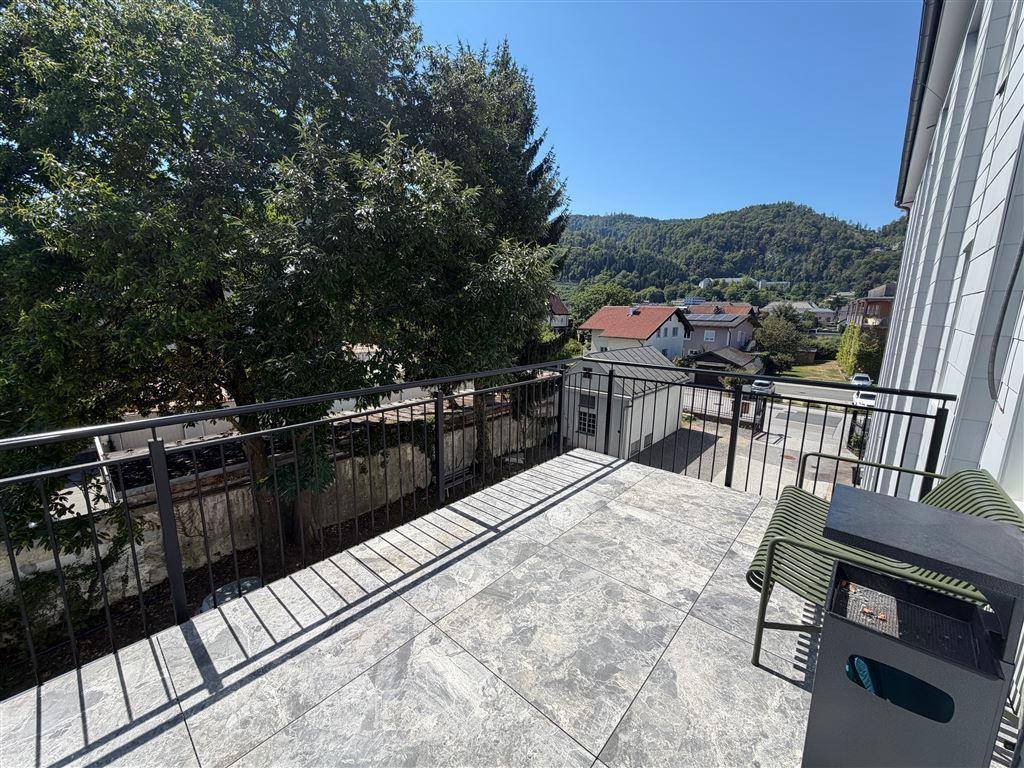Geräumige Terrasse mit Fliesenboden, Metallgeländer und Blick auf Bäume und die umliegende Landschaft.