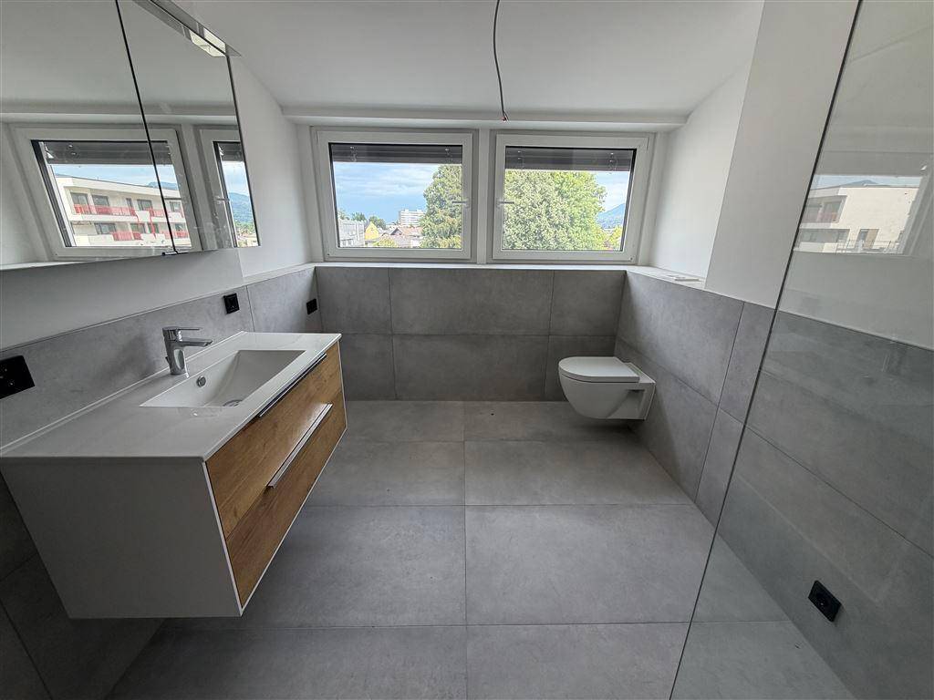 Modernes Badezimmer mit grauen Fliesen, schwebendem Waschtisch und Fenster mit Ausblick.