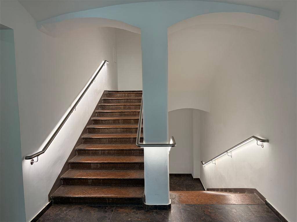 Helles Treppenhaus mit modernen Handläufen und indirekter Beleuchtung, das zu den oberen Etagen führt.