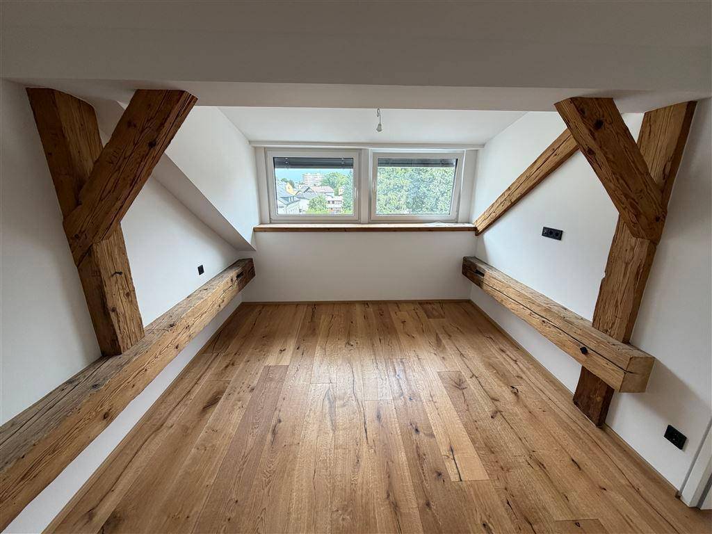 Lichtdurchfluteter Dachbodenraum mit rustikalen Holzbalken und weitem Ausblick durch die Fenster.