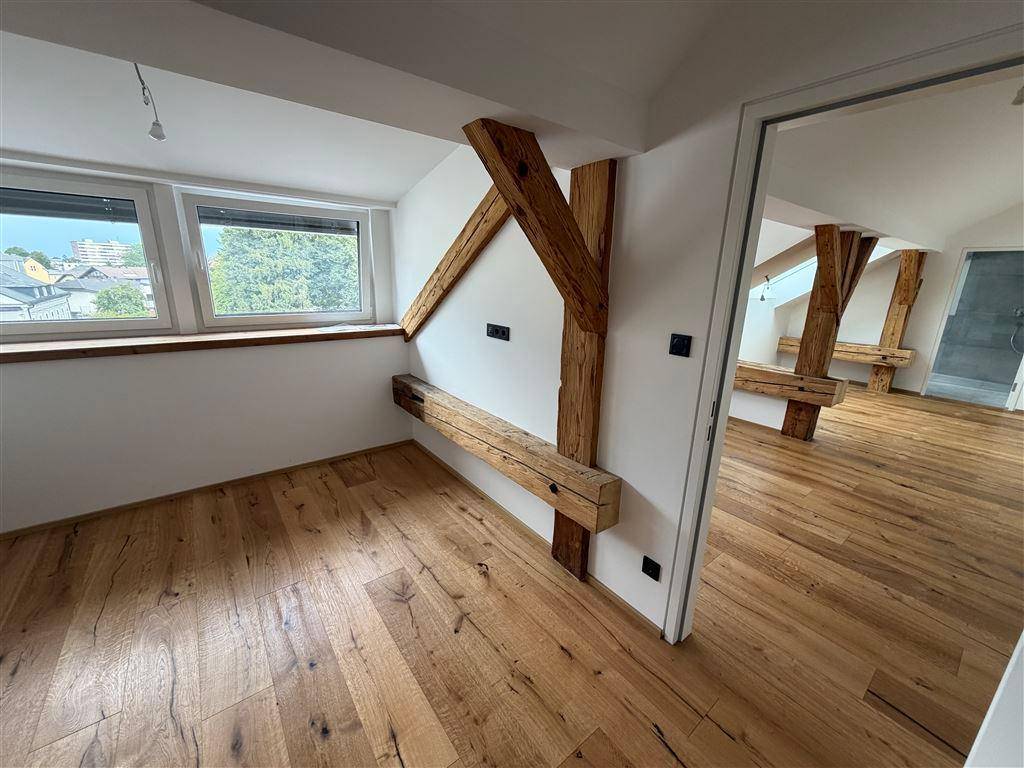 Geräumiger Dachbodenraum mit Holzbalken, Holzboden und Fenstern mit Blick ins Grüne.
