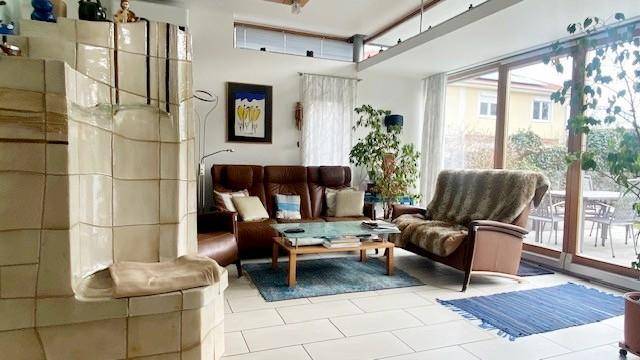 Helles Wohnzimmer mit Kachelofen, Ledersofa und Zugang zur Terrasse mit Gartenblick.