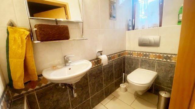 Gäste-WC mit Wand-WC, Waschbecken und Fliesen in verschiedenen Mustern.