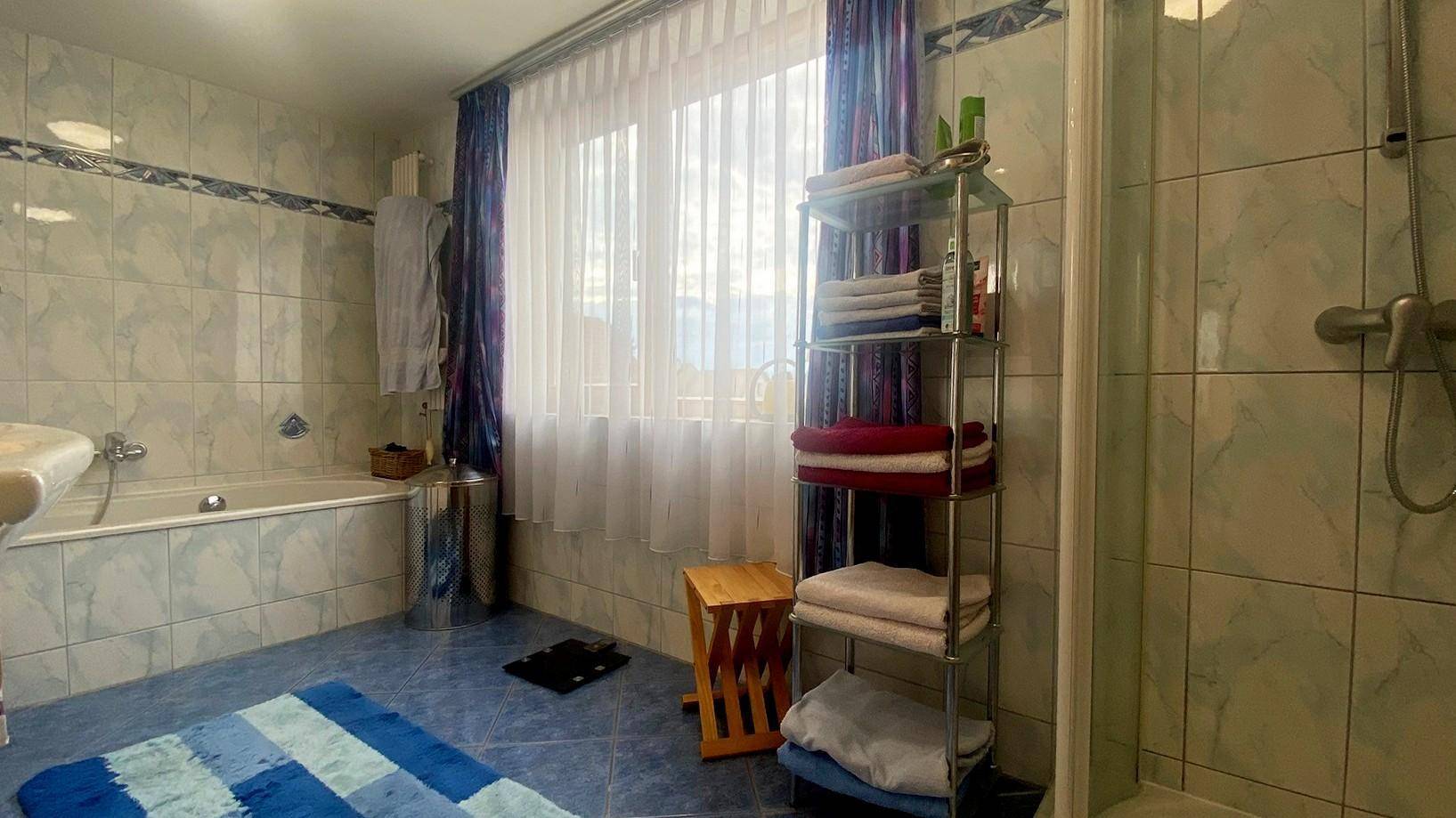 Badezimmer mit Badewanne, Dusche, blauen Fliesen und großem Fenster.