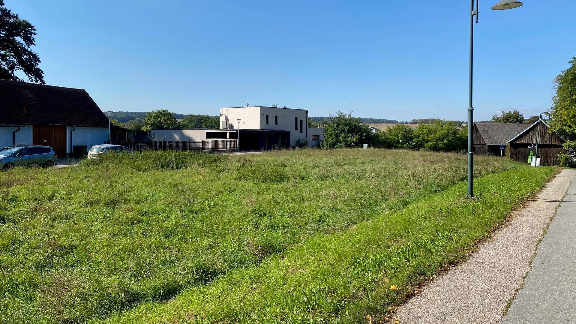 Weitläufiges Grundstück mit Grünfläche, umgeben von bestehenden Gebäuden und einer ruhigen Straße.