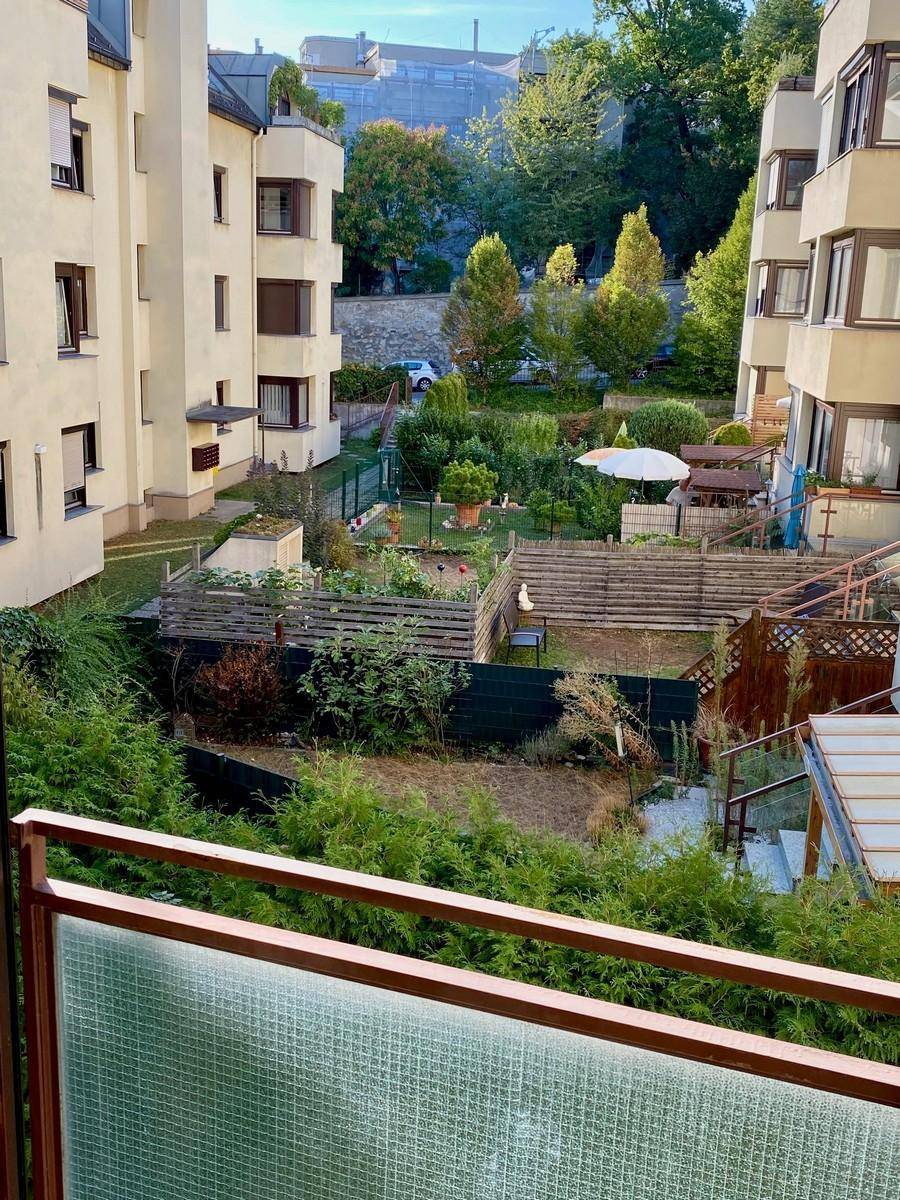 Blick vom Balkon auf den gemeinschaftlichen Gartenbereich mit kleinen Parzellen und umliegenden Gebäuden.