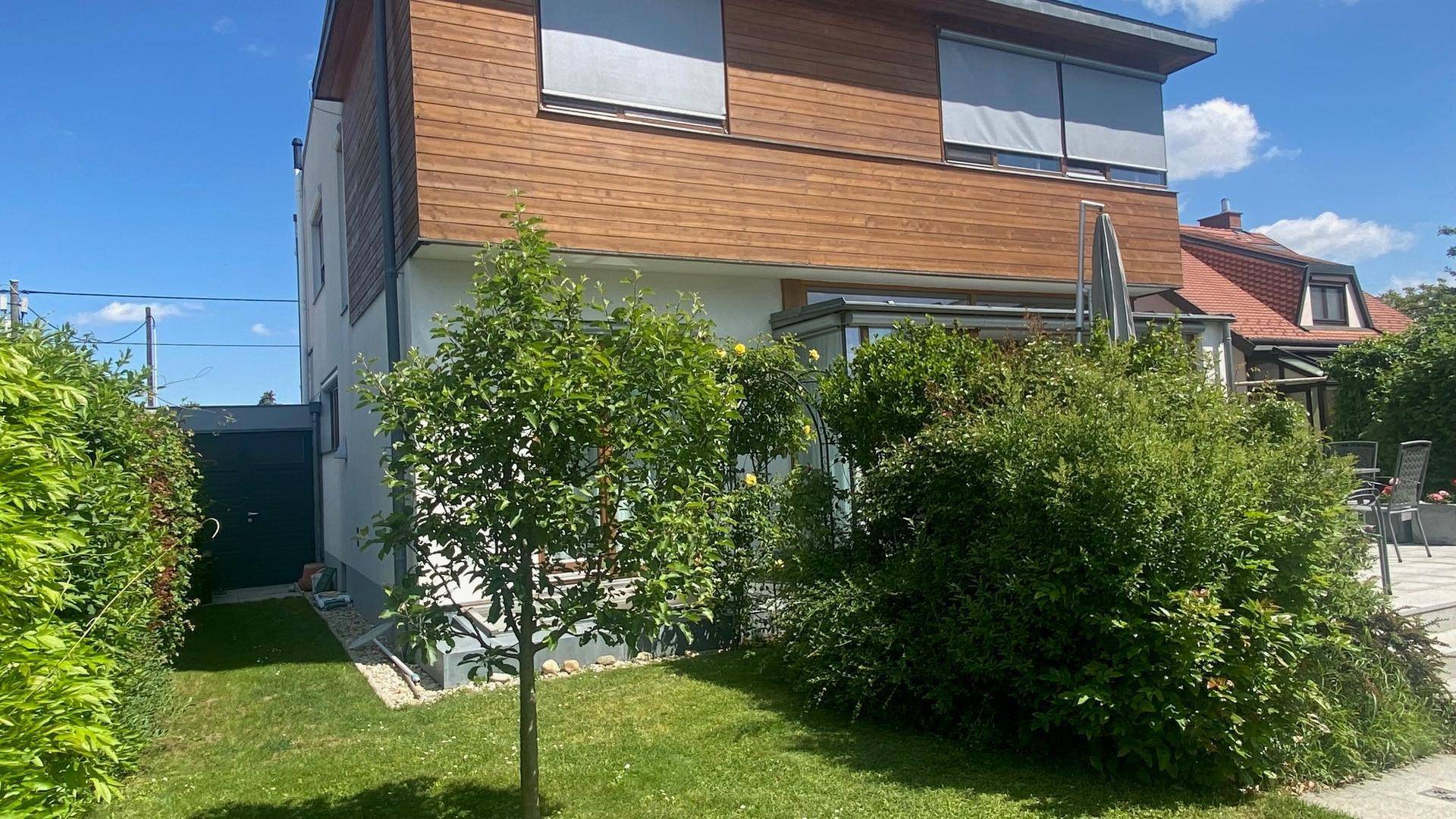 Seitenansicht des Hauses mit Holzfassade, Garten und einem kleinen, grünen Außenbereich.