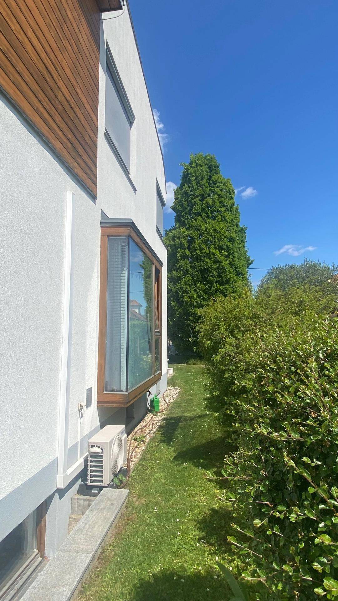 Seitenansicht des Hauses mit Erkerfenster, Klimaanlage und gepflegtem Rasen.