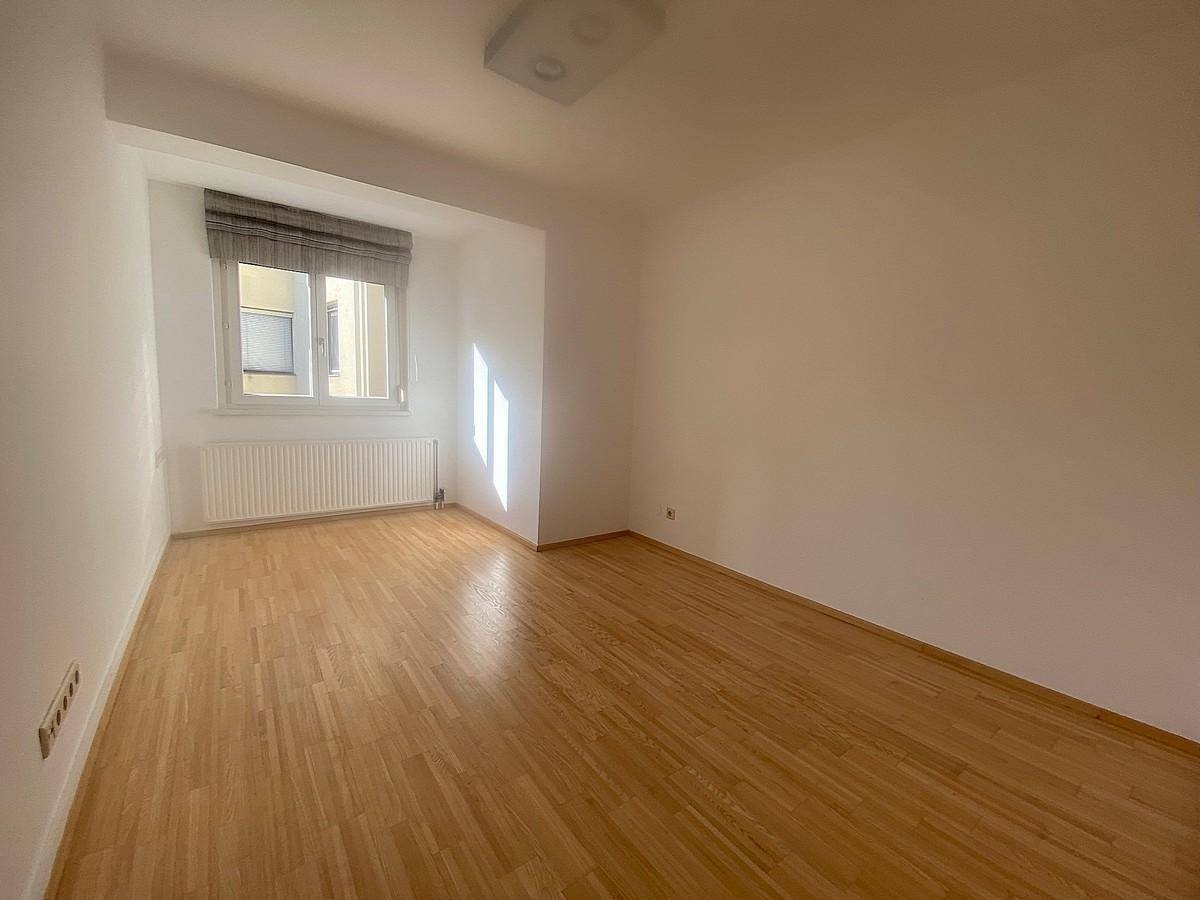 Helles Schlafzimmer mit Parkettboden und einem Fenster, das viel Sonnenlicht hereinlässt.