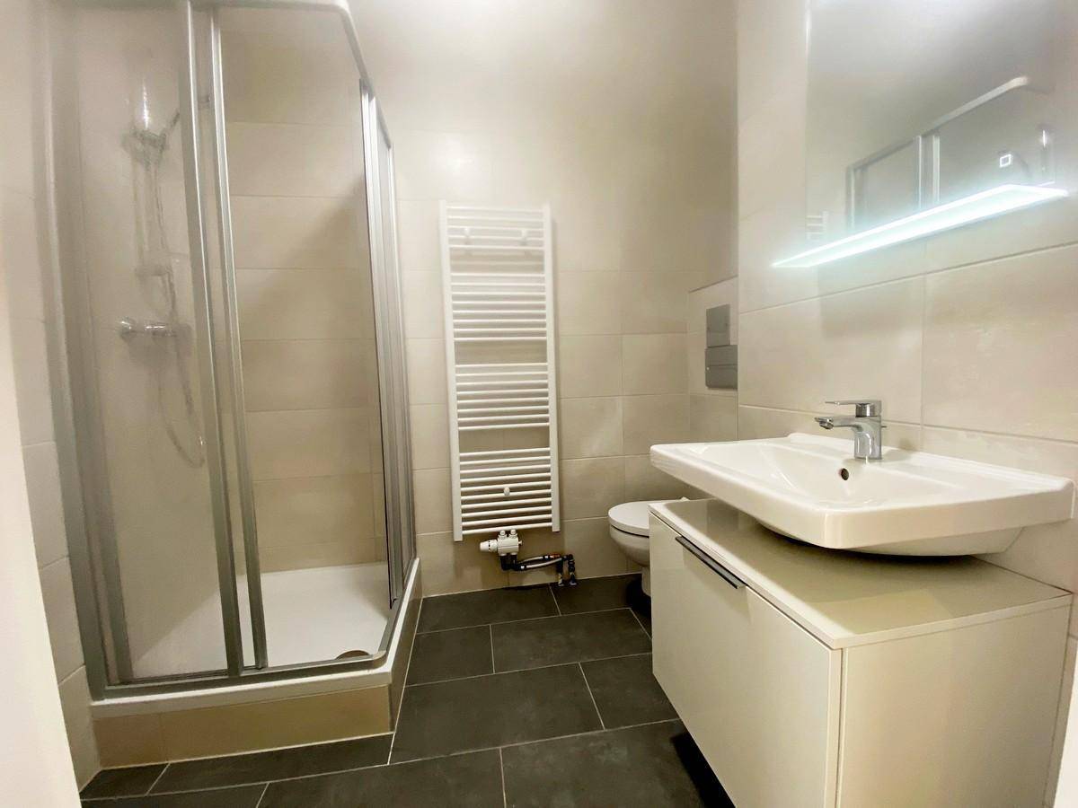 Modernes Badezimmer mit Duschkabine, Waschtisch, WC und beheiztem Handtuchhalter.