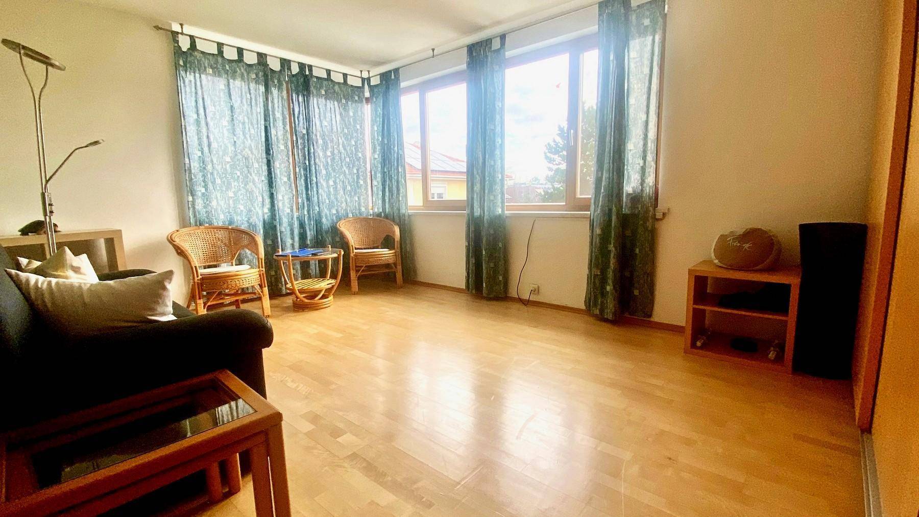 Geräumiges Wohnzimmer mit Holzboden, großen Fenstern und Blick ins Freie.