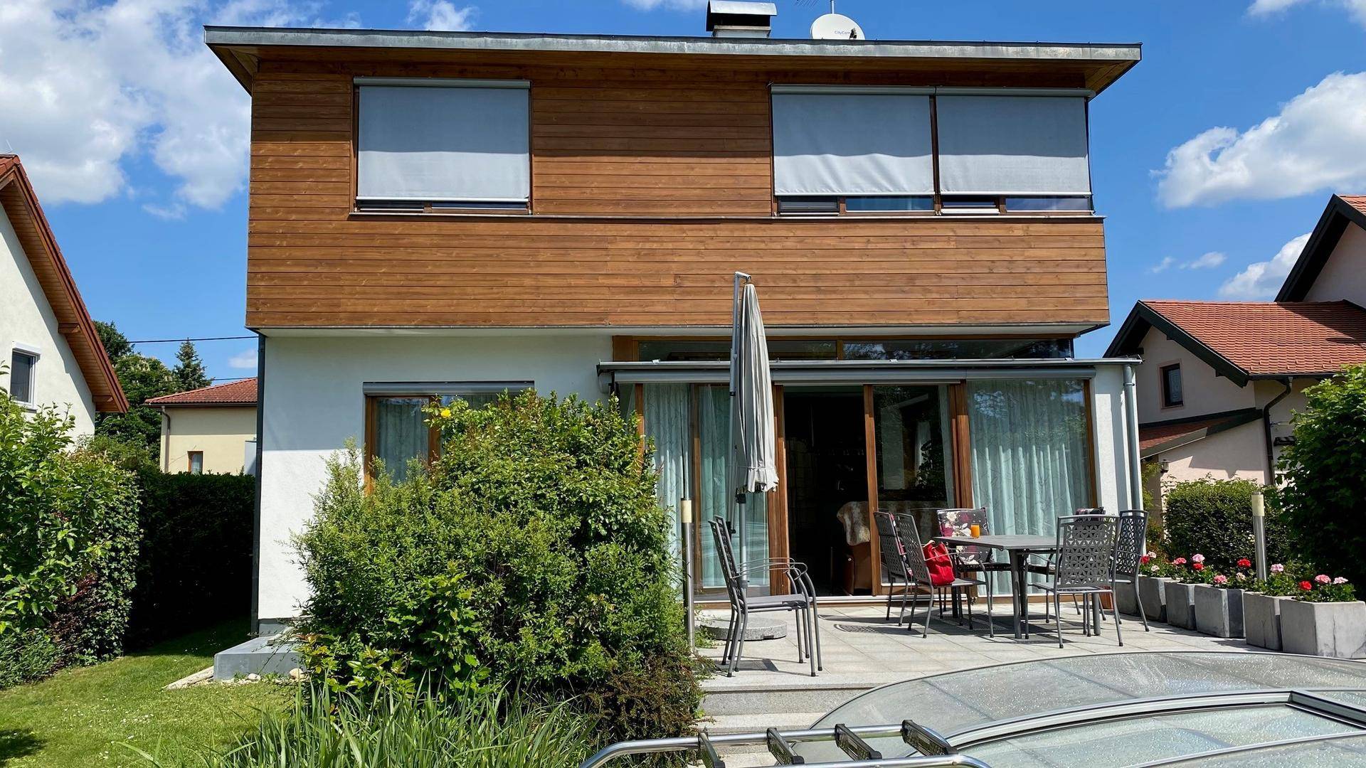 Rückseite des Hauses mit großer Terrasse, Gartenmöbeln und Blick auf den Poolbereich.