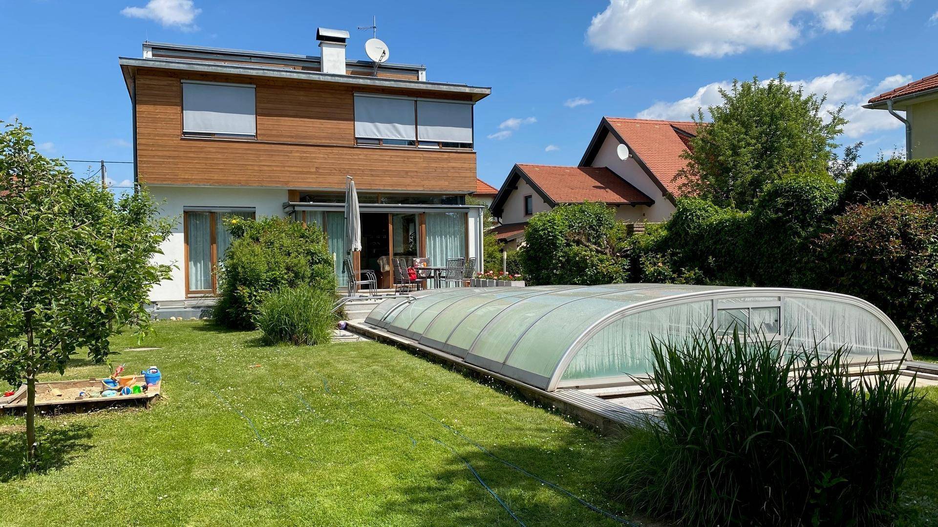 Großer Garten mit überdachtem Pool, Sandkasten und der modernen Hausfassade im Hintergrund.
