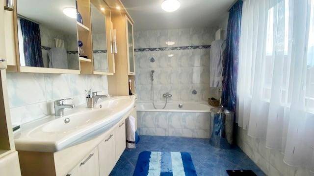 Badezimmer mit Doppelwaschbecken, Badewanne, Spiegelschränken und blauen Fliesen.