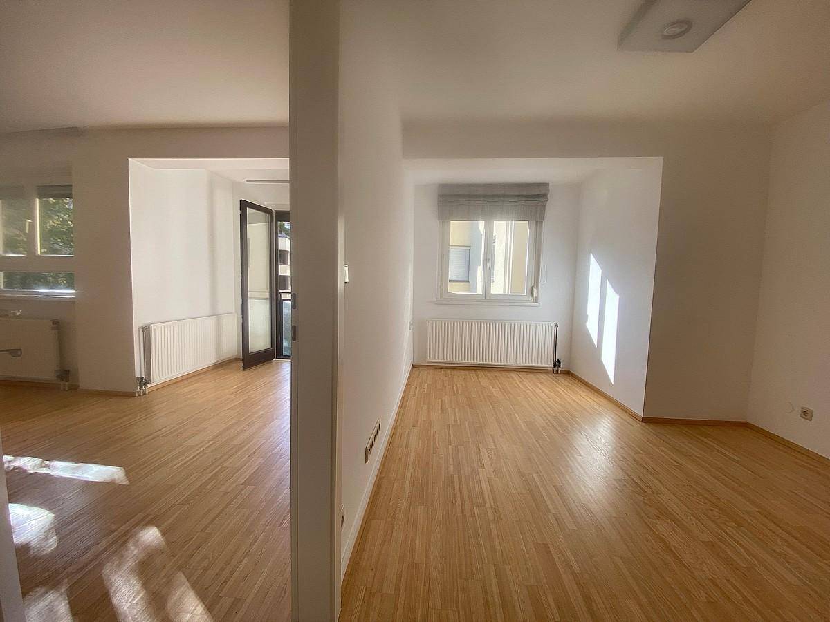 Geräumiger Wohnbereich mit hellem Parkettboden und viel Tageslicht durch mehrere Fenster.