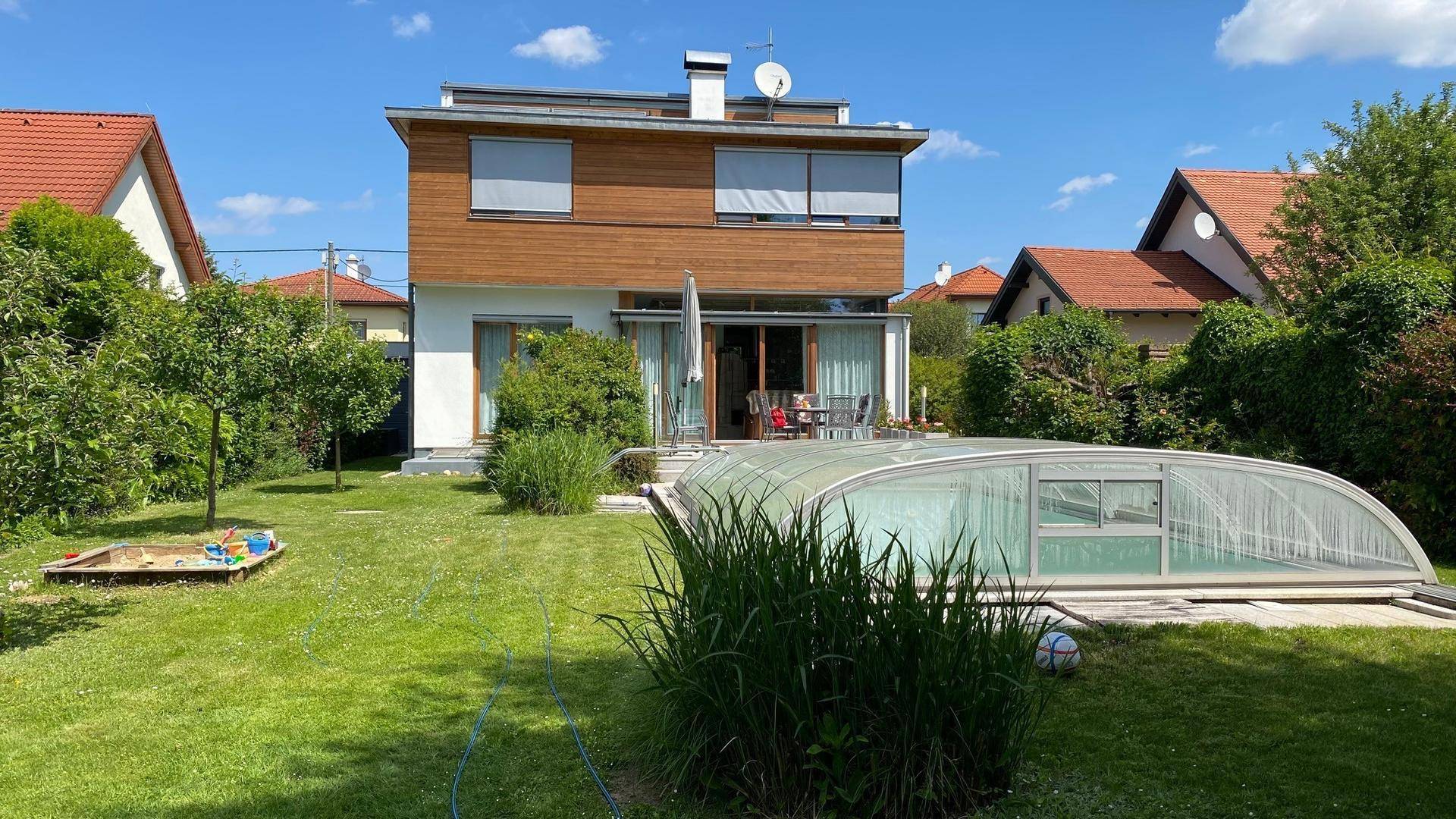 Weitläufiger Garten mit überdachtem Pool und der Rückseite des modernen Hauses.