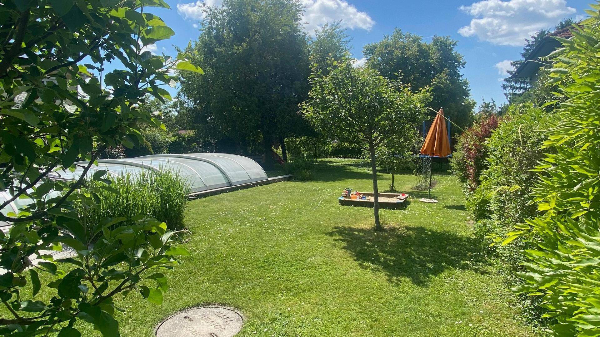 Weitläufiger Garten mit überdachtem Pool, Sandkasten und viel Grünfläche für Freizeitaktivitäten.