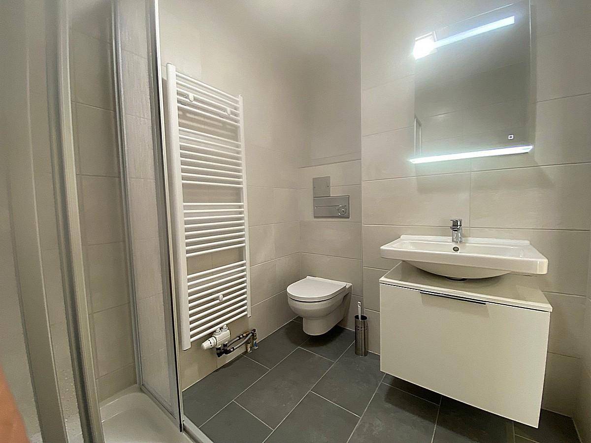 Modernes Badezimmer mit Dusche, Waschtisch, WC und beheiztem Handtuchhalter in hellen Tönen.