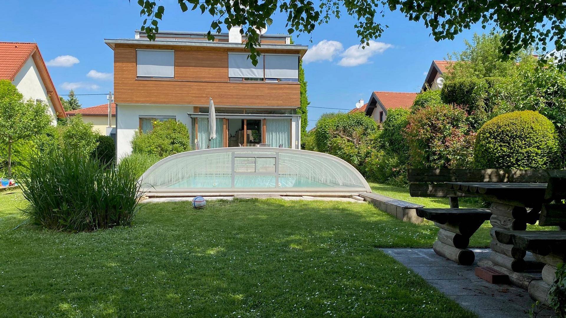 Sonniger Garten mit überdachtem Pool und rustikaler Holzbankgarnitur für entspannte Stunden.