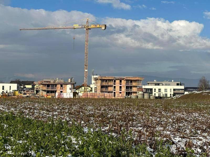 Baustelle einer Wohnanlage mit Kran und Rohbauten unter bewölktem Himmel.