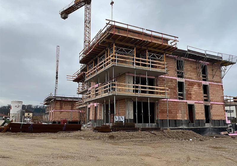 Nahaufnahme einer Baustelle mit Rohbauten, Schalungen und einem Baukran im Hintergrund.