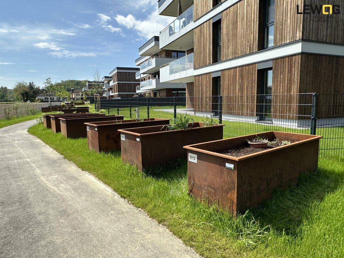 Außenbereich der Wohnanlage mit modernen Pflanzkübeln und gepflegtem Rasen.
