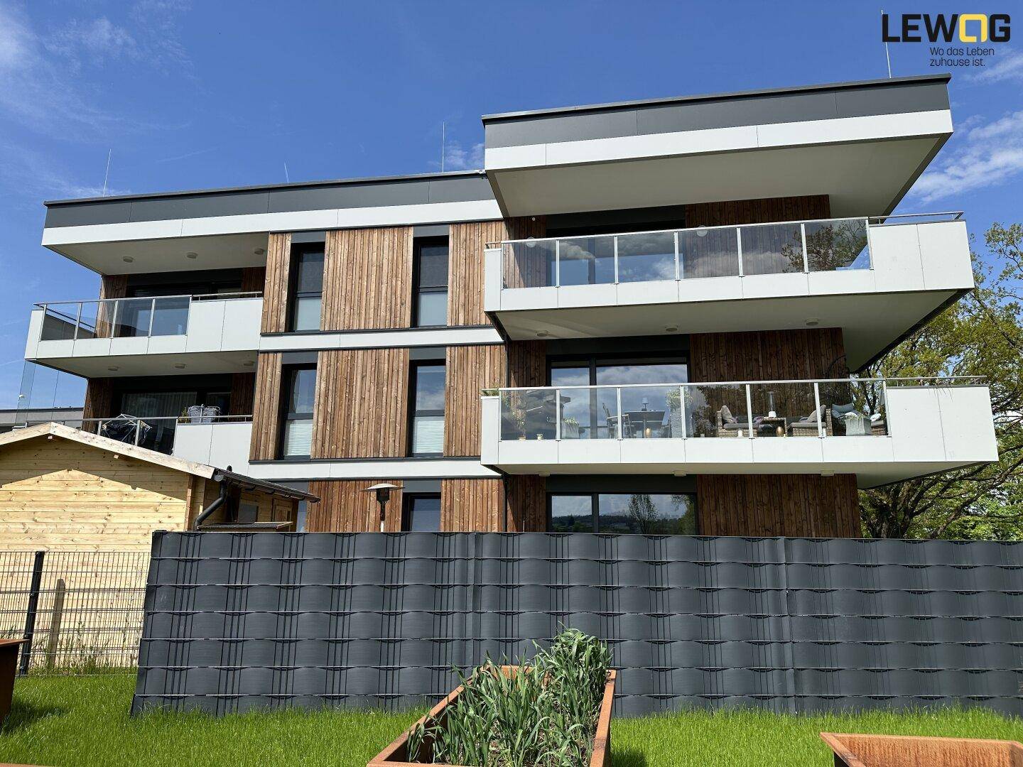 Moderne Wohnanlage mit Holzfassade, großen Balkonen und Glasgeländern.